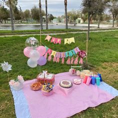 a picnic table set up with balloons, cake and snacks