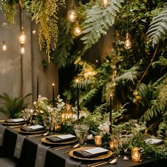 a long table set with black and gold place settings, greenery and hanging lights