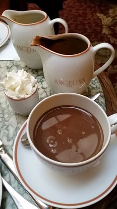 there is a cup of hot chocolate on the table with other cups and spoons