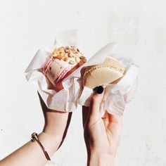 a person holding up a sandwich in their left hand, with the rest of the sandwich wrapped in tissue paper