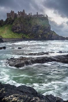 a castle on top of a hill next to the ocean with waves crashing in front of it