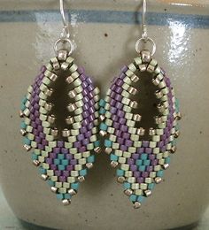 a pair of purple and blue beaded earrings sitting on top of a white vase