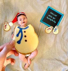 a baby in a santa hat is holding a cookie with an image of a snowman on it