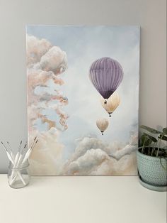 two hot air balloons flying in the sky with clouds behind them on a white shelf next to a potted plant