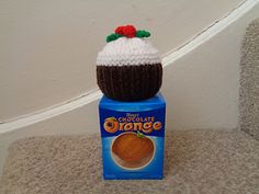 a crocheted hat sitting on top of a carton of orange juice next to a wall