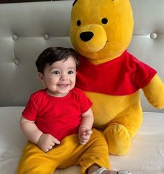 a small child sitting next to a large stuffed winnie the pooh bear on a bed