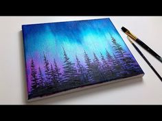 an art journal with trees painted on it and two paintbrushes next to it