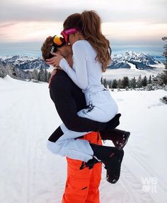 a man holding a woman on his back while standing in the snow with mountains in the background