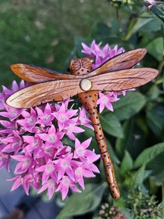 a wooden dragon sitting on top of a purple flower next to some green leaves and pink flowers