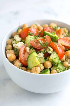 a white bowl filled with chickpeas, tomatoes and cucumbers