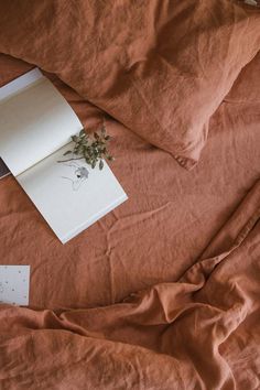 an open book on top of a bed covered in brown sheets and linens with a plant growing out of it