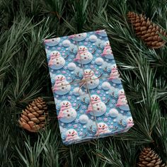 a wrapping paper with snowmen and pine cones in the foreground, on top of evergreen branches