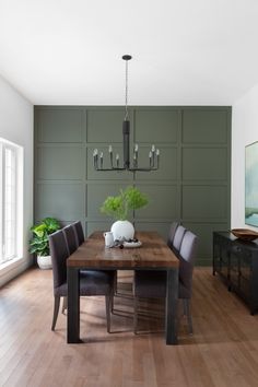 a dining room table with chairs and a vase on top of it, in front of a green paneled wall