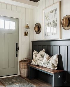 a bench with pillows on it in front of a door and some pictures above it