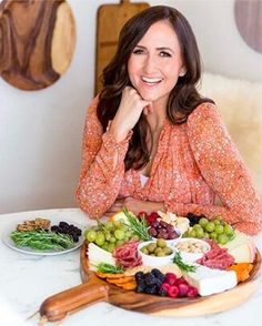 a woman sitting at a table with a platter of cheese and fruit on it