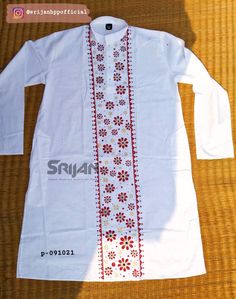 an embroidered white shirt with red flowers on the front and side, sitting on a wooden surface