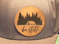 a hat with a patch on it that says be still in front of some trees