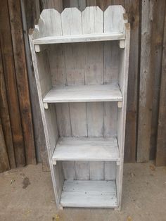 an old white bookcase is sitting in front of a wooden fence and wood planks