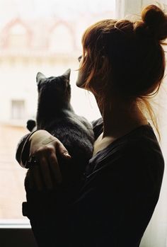 a woman holding a cat in front of a window