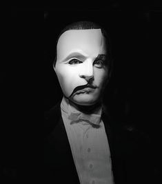 a man in a suit and mask with his face partially obscured by a black background