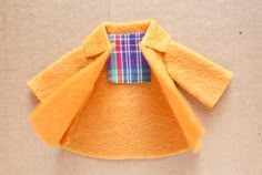 an orange coat with a plaid pocket on the collar is laying on top of a brown surface