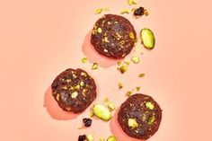 three pieces of chocolate and pistachio cookies on a pink background with scattered seeds