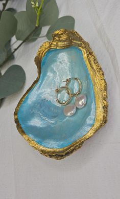 two wedding rings are placed in a blue agate shell with gold leafy branches