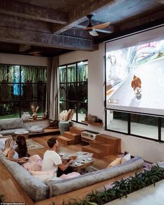 two people sitting on couches in front of a flat screen tv that is mounted to the wall