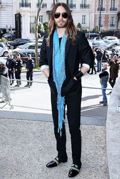 a man with long hair wearing sunglasses and a blue scarf standing in front of a building