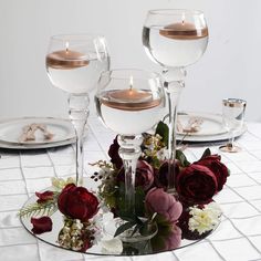 there are three wine glasses on the table with flowers and candles in them as centerpieces