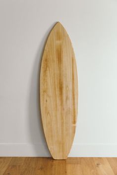 a wooden surfboard leaning up against a wall in a room with hard wood flooring