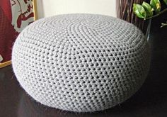 a crocheted ottoman sitting on top of a table next to a vase with flowers