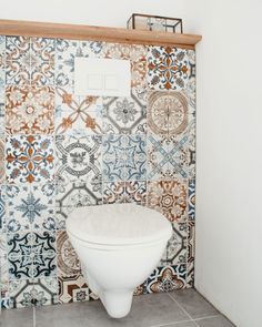 a white toilet sitting inside of a bathroom next to a wall covered in colorful tiles