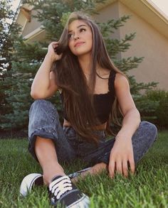 a young woman sitting on the grass in front of a house smiling at the camera