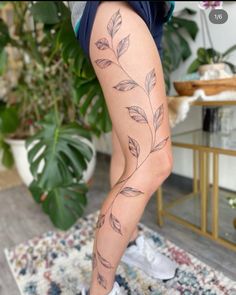 a woman with tattoos on her legs and leggings is standing in front of a potted plant