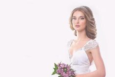 a woman in a white wedding dress holding a purple bouquet and looking at the camera