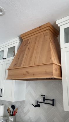 a kitchen with white cabinets and wood stove hood