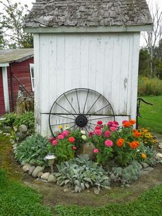 an old wheel sits in the middle of a garden with flowers and plants around it