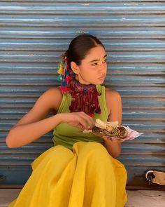 a woman sitting on the ground with food in her hand and wearing a scarf around her neck