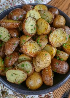 a bowl filled with cooked potatoes on top of a wooden table next to a napkin