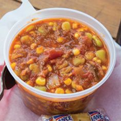 a bowl of chili with corn on the side next to a bag of chips and a drink