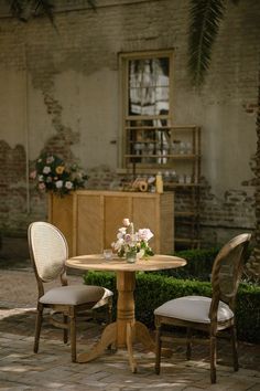 two chairs and a table with flowers on it in the middle of a courtyard area