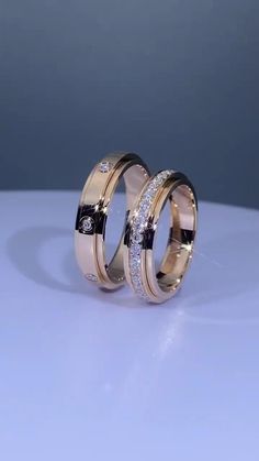 two gold wedding rings with diamonds on them sitting on a white surface, against a blue background