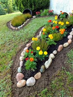 a garden with flowers and rocks in the middle of it, along side a house