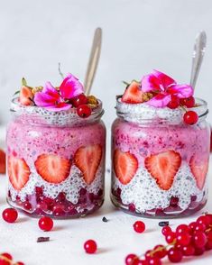 two mason jars with strawberries and flowers in them on a white surface surrounded by berries