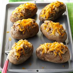 six baked potatoes with cheese on top sitting on a baking sheet next to a knife and fork