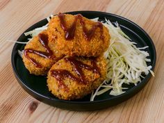 two fried food items on a black plate with coleslaw and slaw in the background