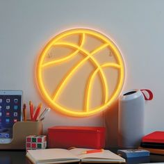 an illuminated basketball ball on the wall above a desk with books, pencils and pens