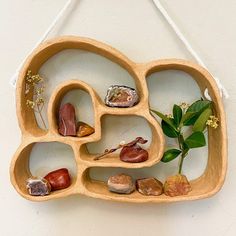 a wooden shelf with various rocks and plants on the top, hanging from a rope