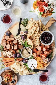 a platter filled with meats, vegetables and crackers next to glasses of wine